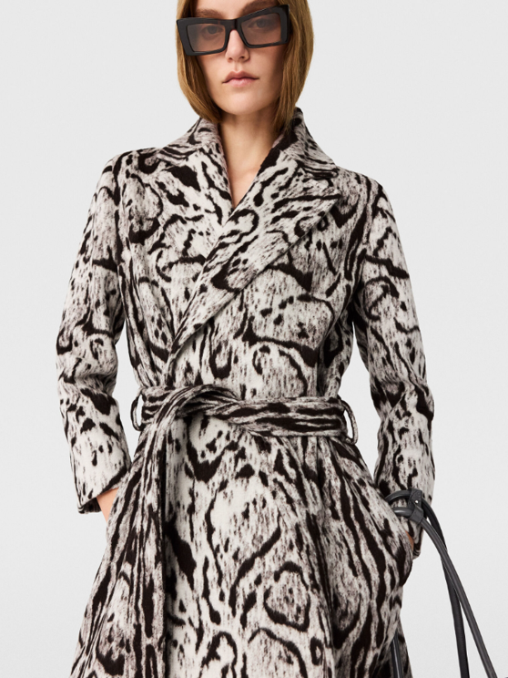 Woman wearing a black and white animal print coat with a matching belt, large black sunglasses, and holding a black handbag.
