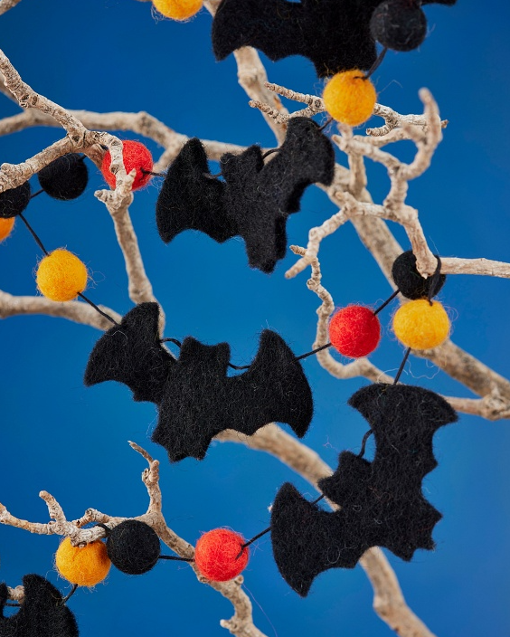 Decorative Halloween garland with black bats and colorful balls on a twisted white branch against a blue background.