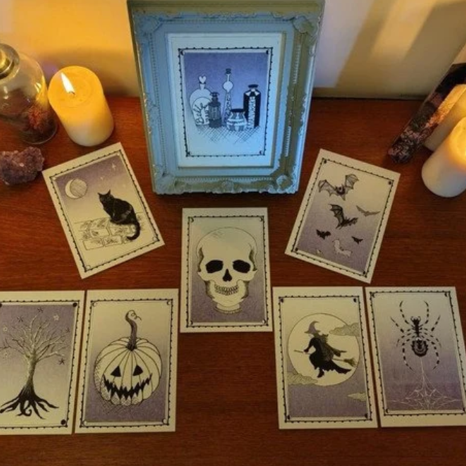 A framed picture of bottles and jars. Seven tarot cards featuring spooky images like a black cat, a skull, bats, a pumpkin with a face, a witch on a broomstick, and a spiderweb with a spider. Four candles and a jar on a wooden surface.
