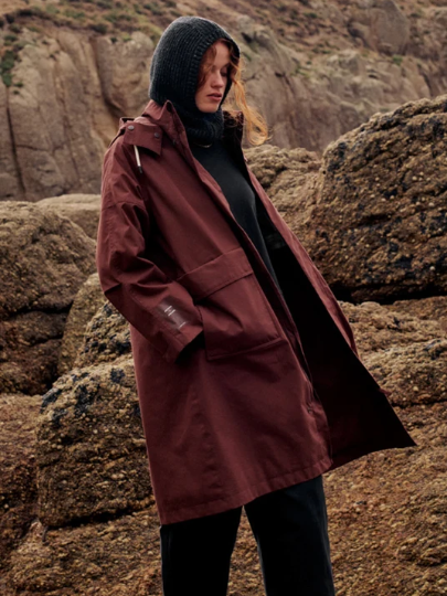 Woman wearing a maroon jacket and black hoodie, standing against rocky terrain