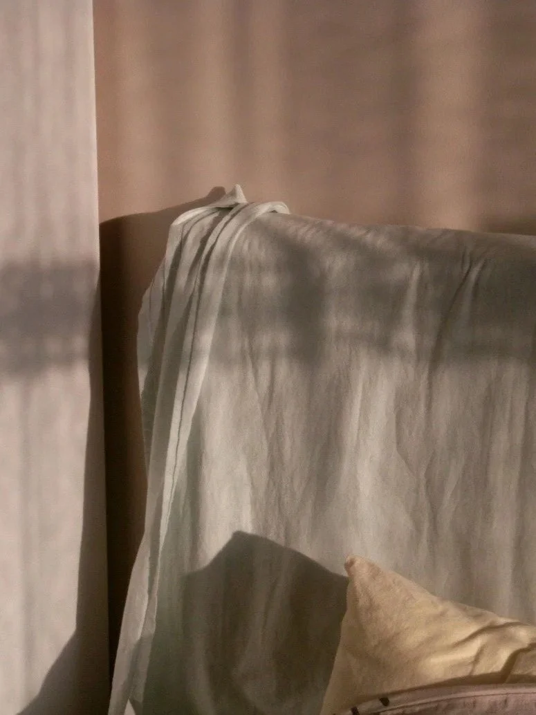 Part of a beige sofa with a cream-colored throw blanket draped over the backrest, against a matching beige wall.
