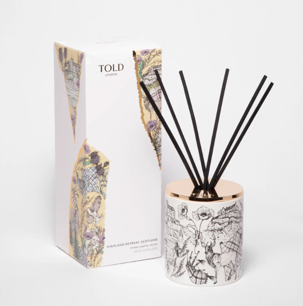 A decorative reed diffuser with a white ceramic base featuring black line art of animals and plants, topped with a metallic rose gold lid, next to its packaging box with a colorful abstract pattern.