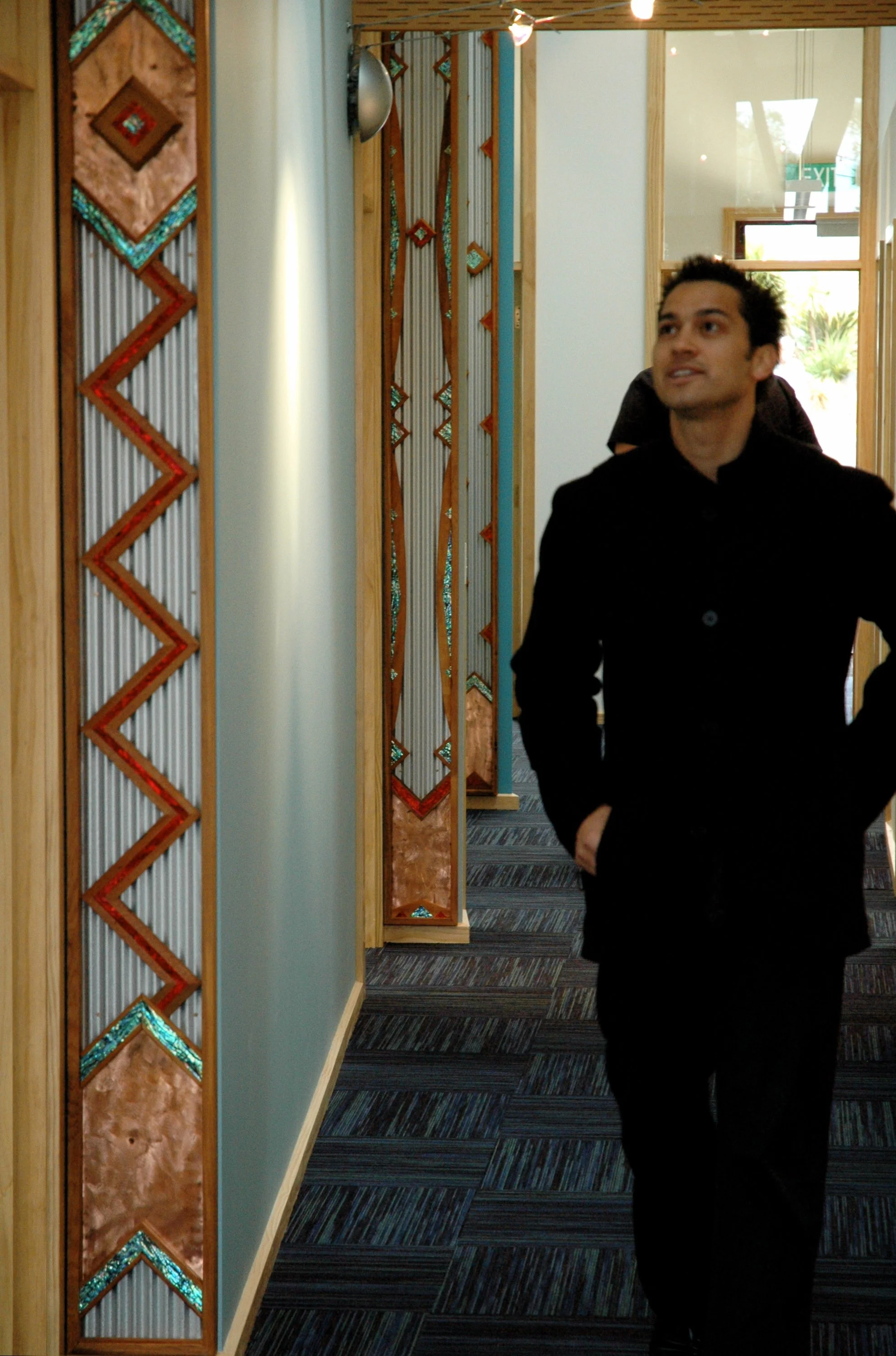 Man walking up a hallway featuring Māori carving details on the wall