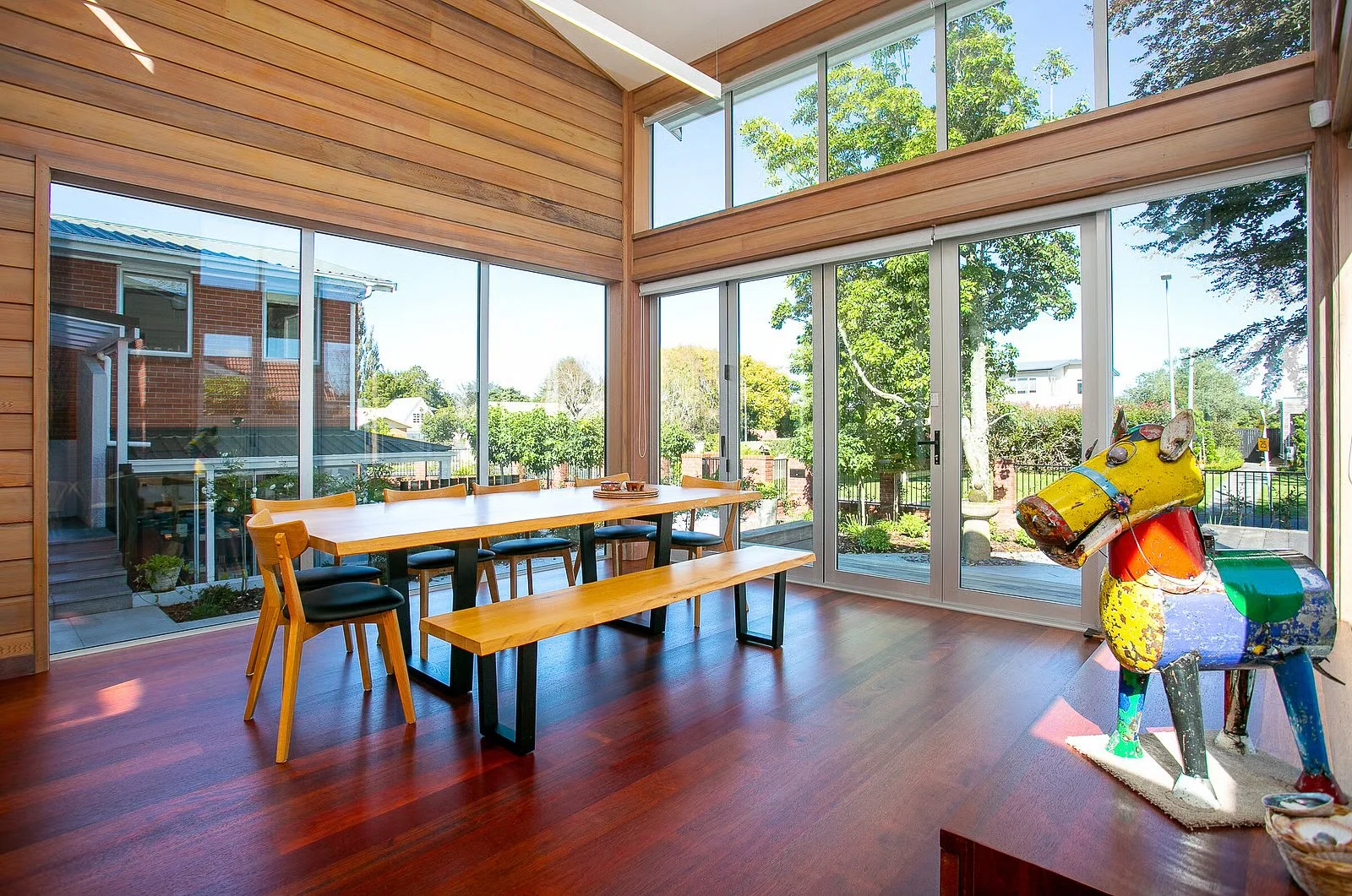 Yellow dining table, high ceilings, big windows and doors looking outside of the dining room