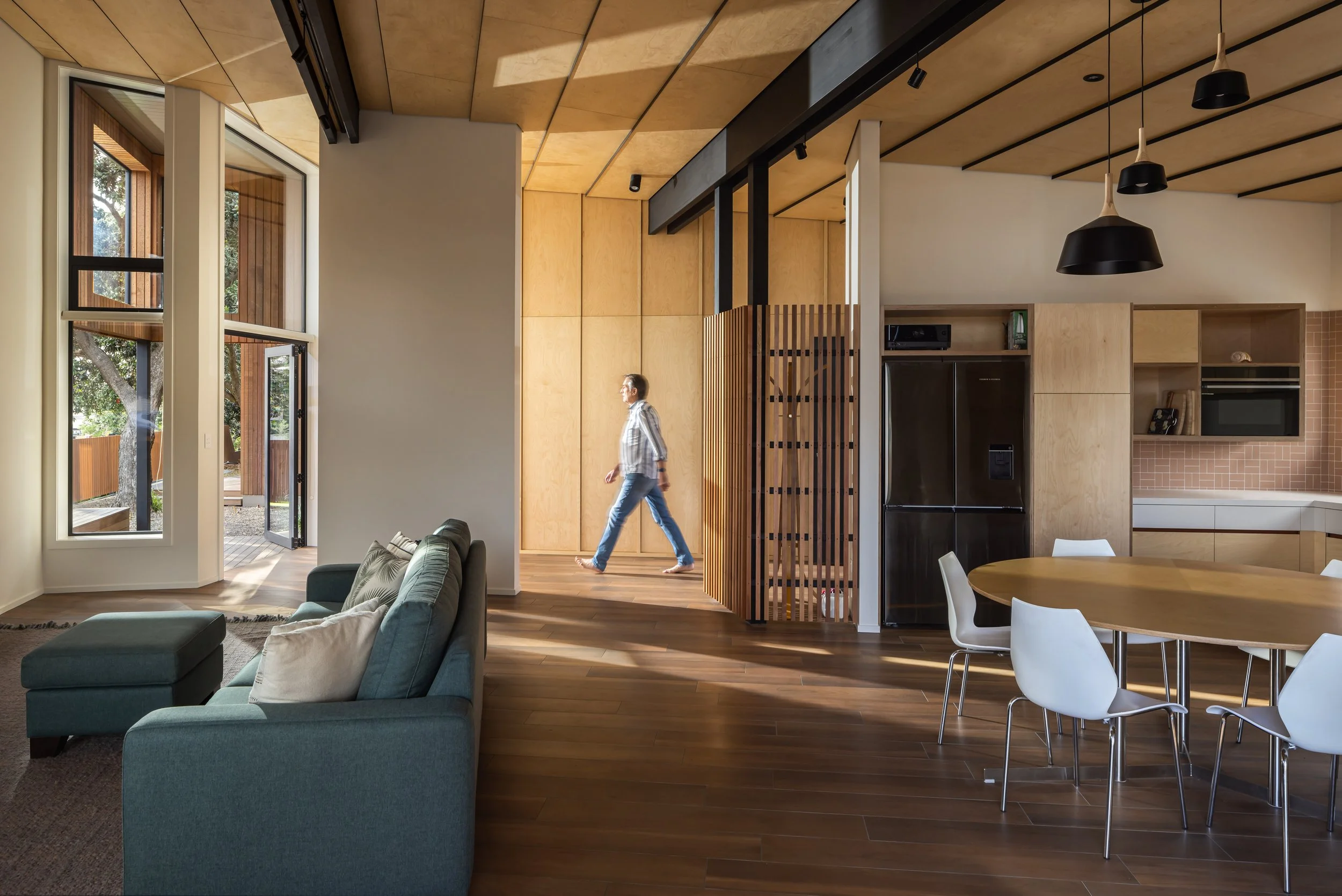 Pōhutukawa House indoor living and dining area with person walking up the hallway to the front door