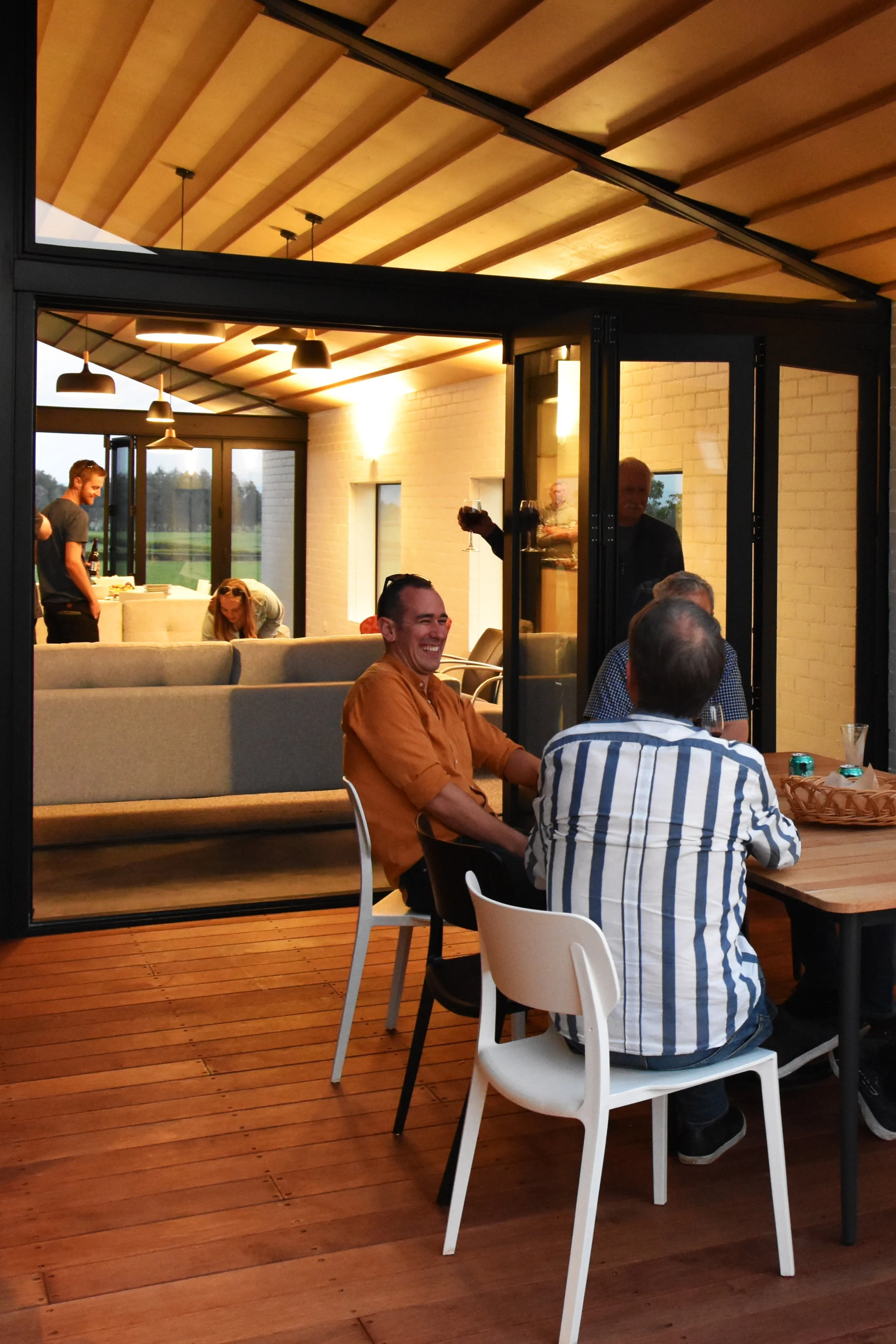 People laughing and catching up together in a well lit Pencarrow house with indoor-outdoor flow deck evening