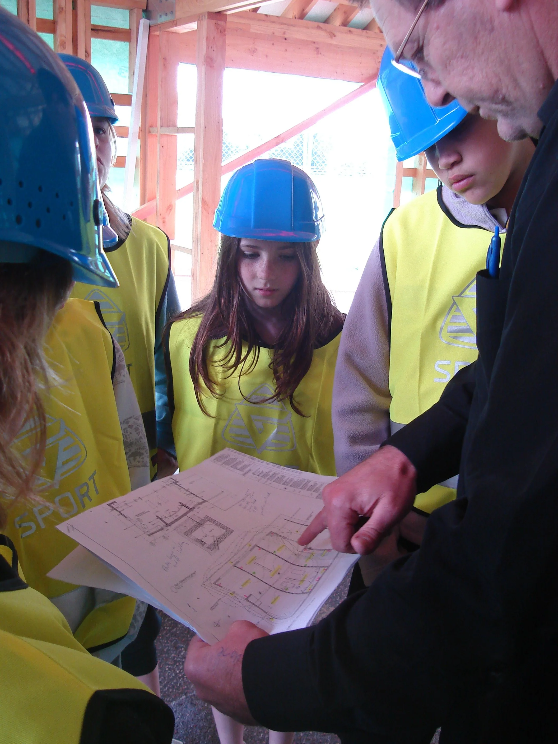 A group of people of various ages working in collaboration on a building site inspecting plans