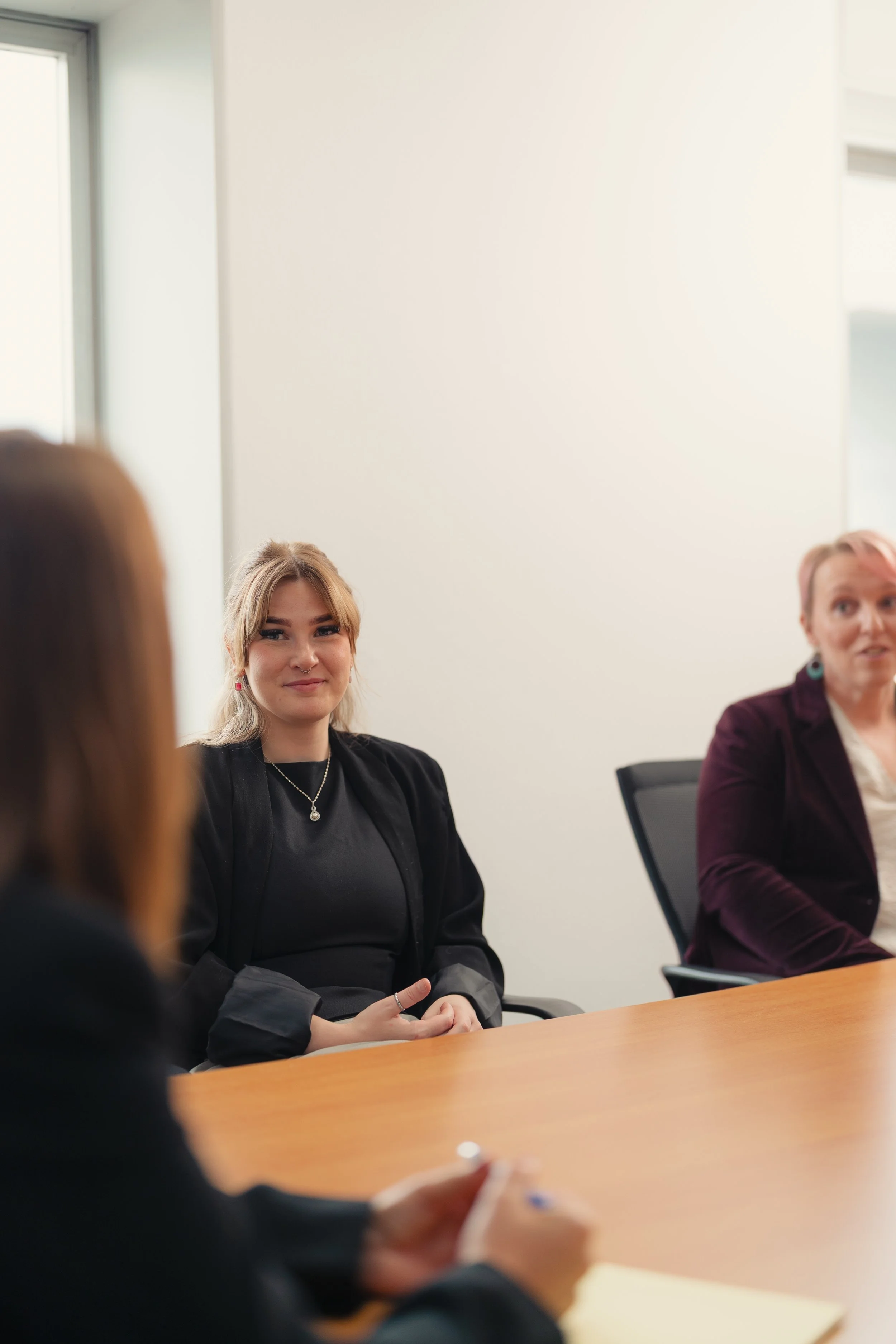 Three women sitting at a conference table in a meeting room, with one woman smiling and looking at the camera.