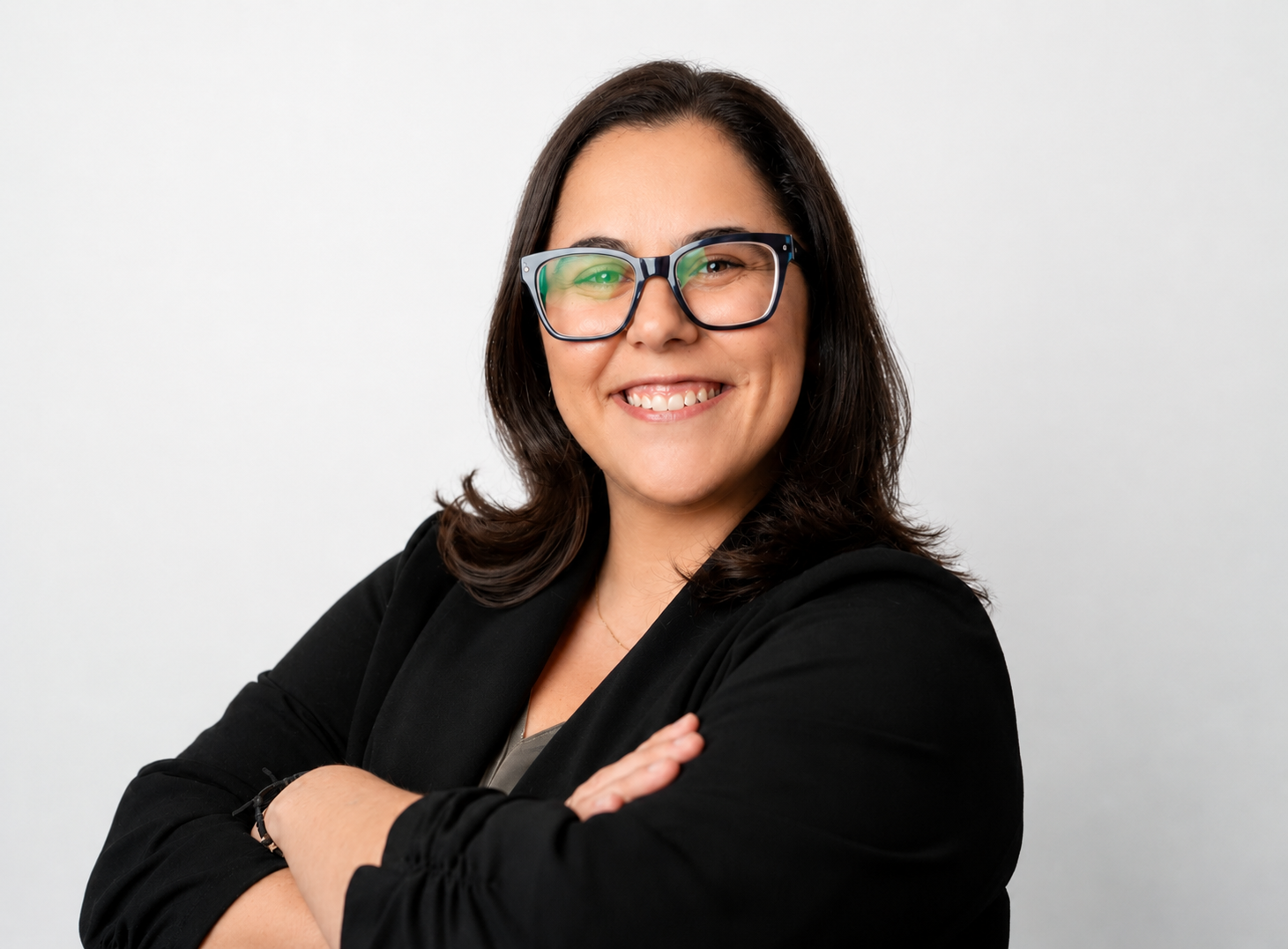 A smiling woman with dark hair wearing glasses and a black jacket standing against a white background.