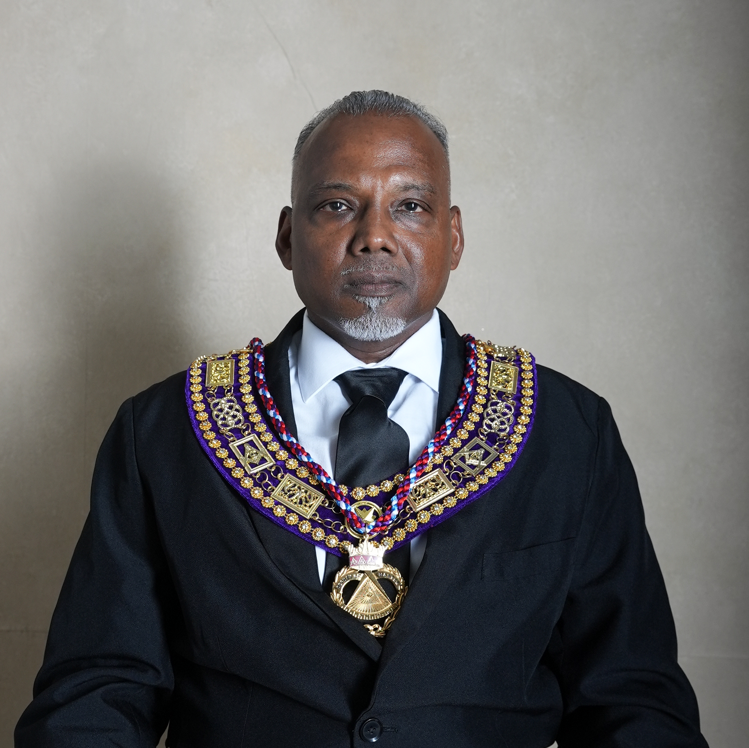 Man in formal attire wearing ceremonial regalia with gold and purple accents, standing against a white background, with text below reading "Jerry Shakur, RWDEGM".