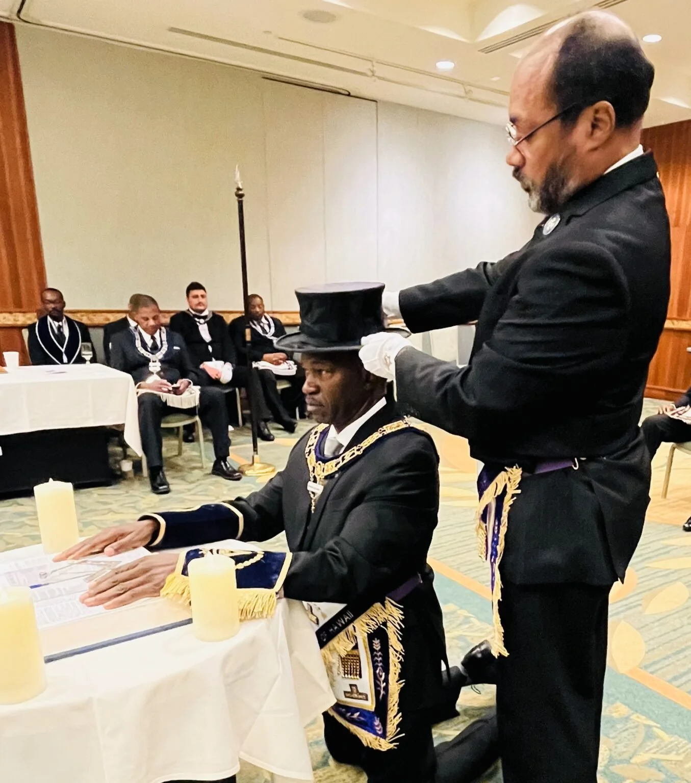 A Masonic initiation or ceremony with men dressed in formal Masonic regalia, including sashes, medals, and aprons, in a decorated indoor setting.