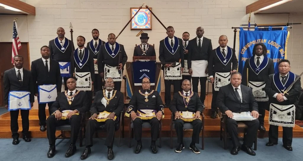 Group of men in tuxedos and Masonic regalia posing in a lodge room with American flag and Masonic banners.
