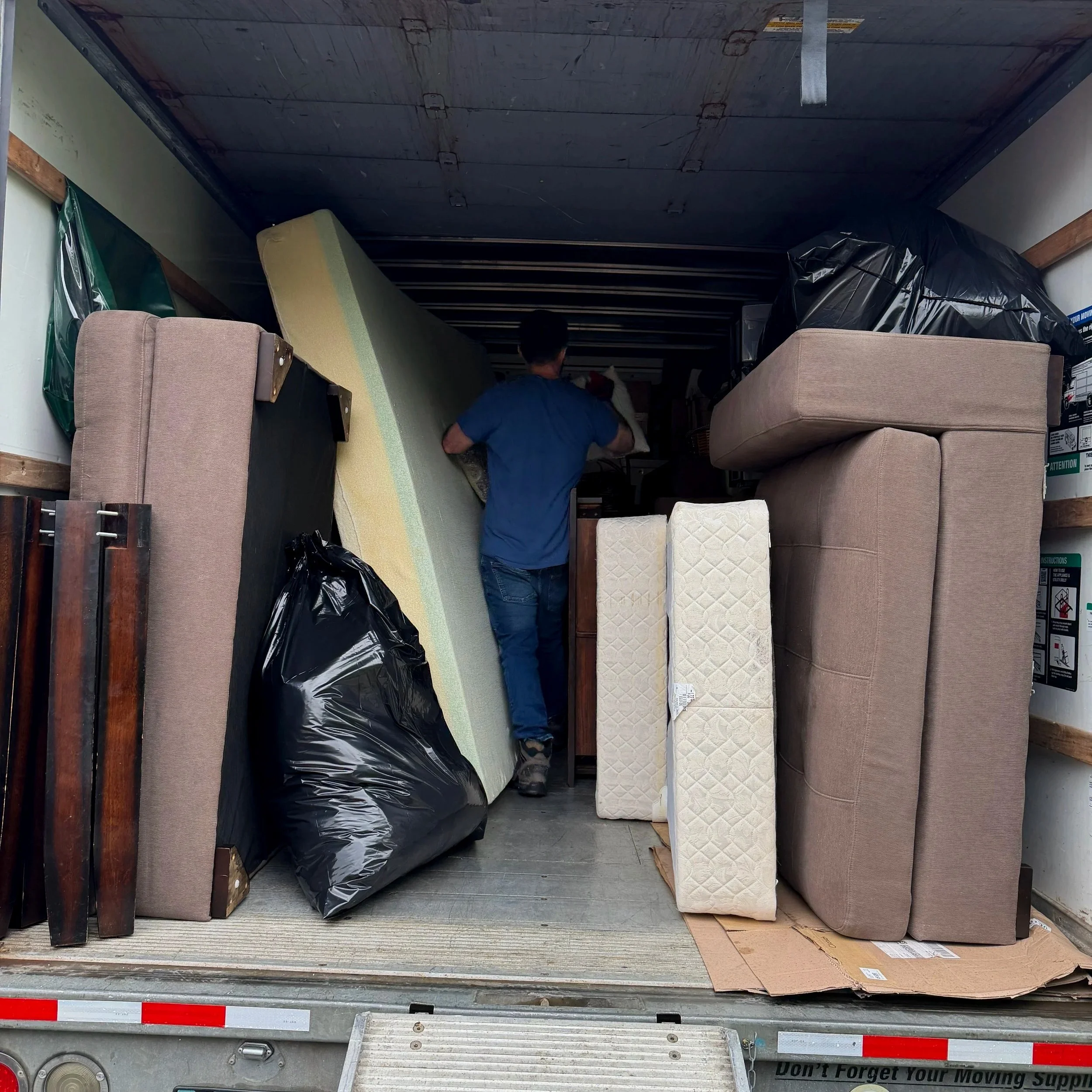 A moving truck filled with furniture and household items, including mattresses, chairs, and boxes.