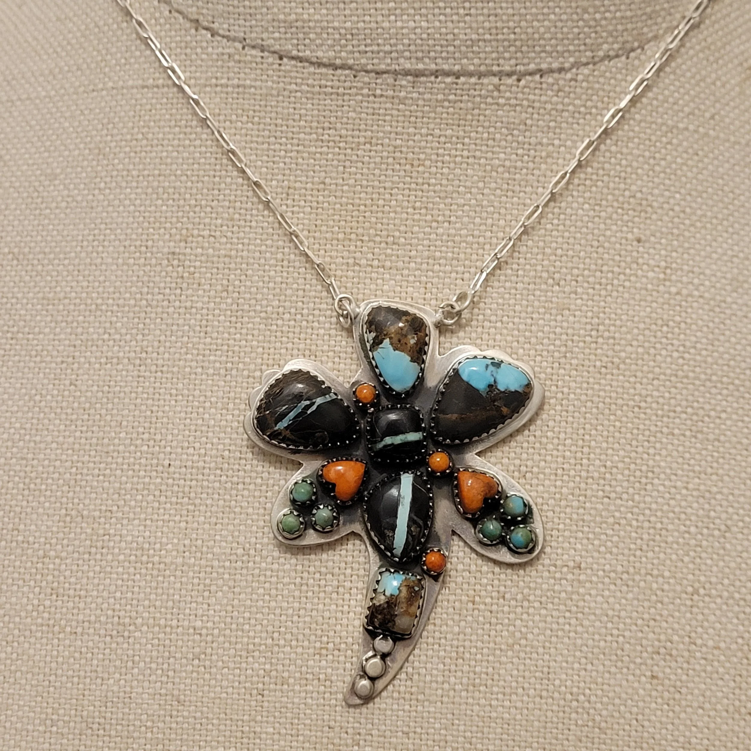 A silver butterfly-shaped pendant necklace with colorful semi-precious stones displayed on a beige fabric background.