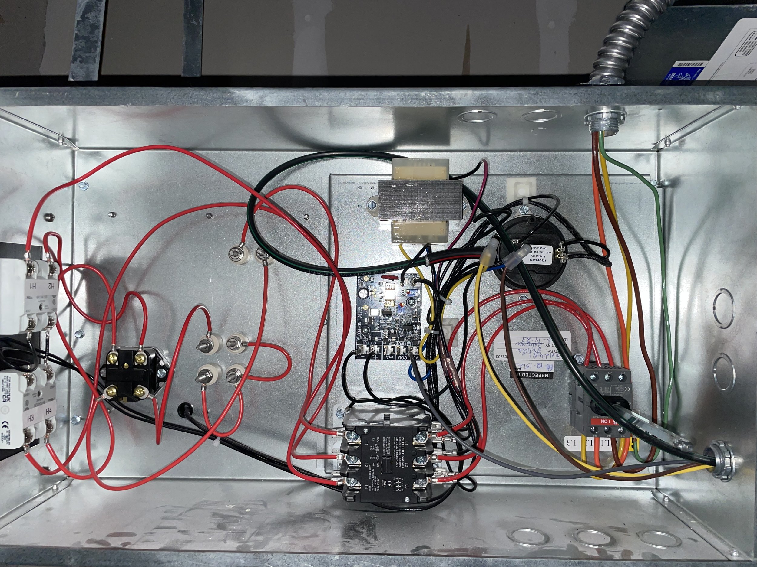 Electrical control panel with wiring, relays, and electronic components inside a metal enclosure.