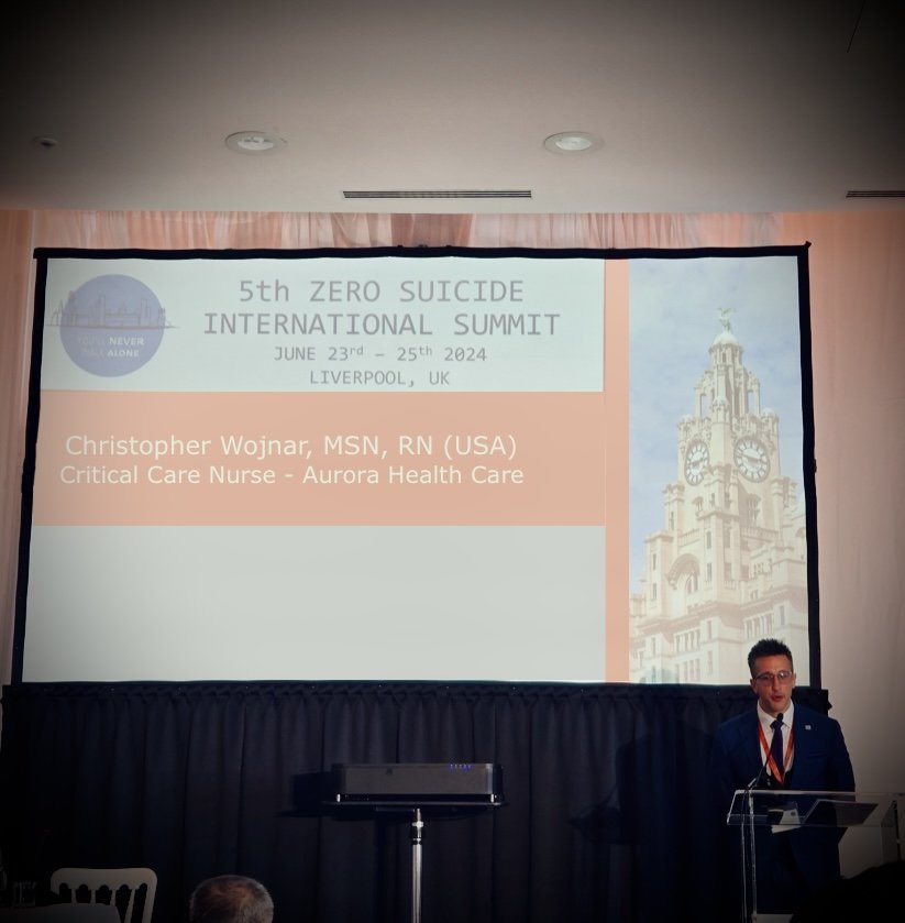 Presentation slide for the 5th Zero Suicide International Summit, taking place from June 23rd to 25th, 2024 in Liverpool, UK. The slide displays the name of speaker Christopher Wojnjar, MSN, RN (USA), Critical Care Nurse at Aurora Health Care, with a partial image of a historic building with clocks on the right side.