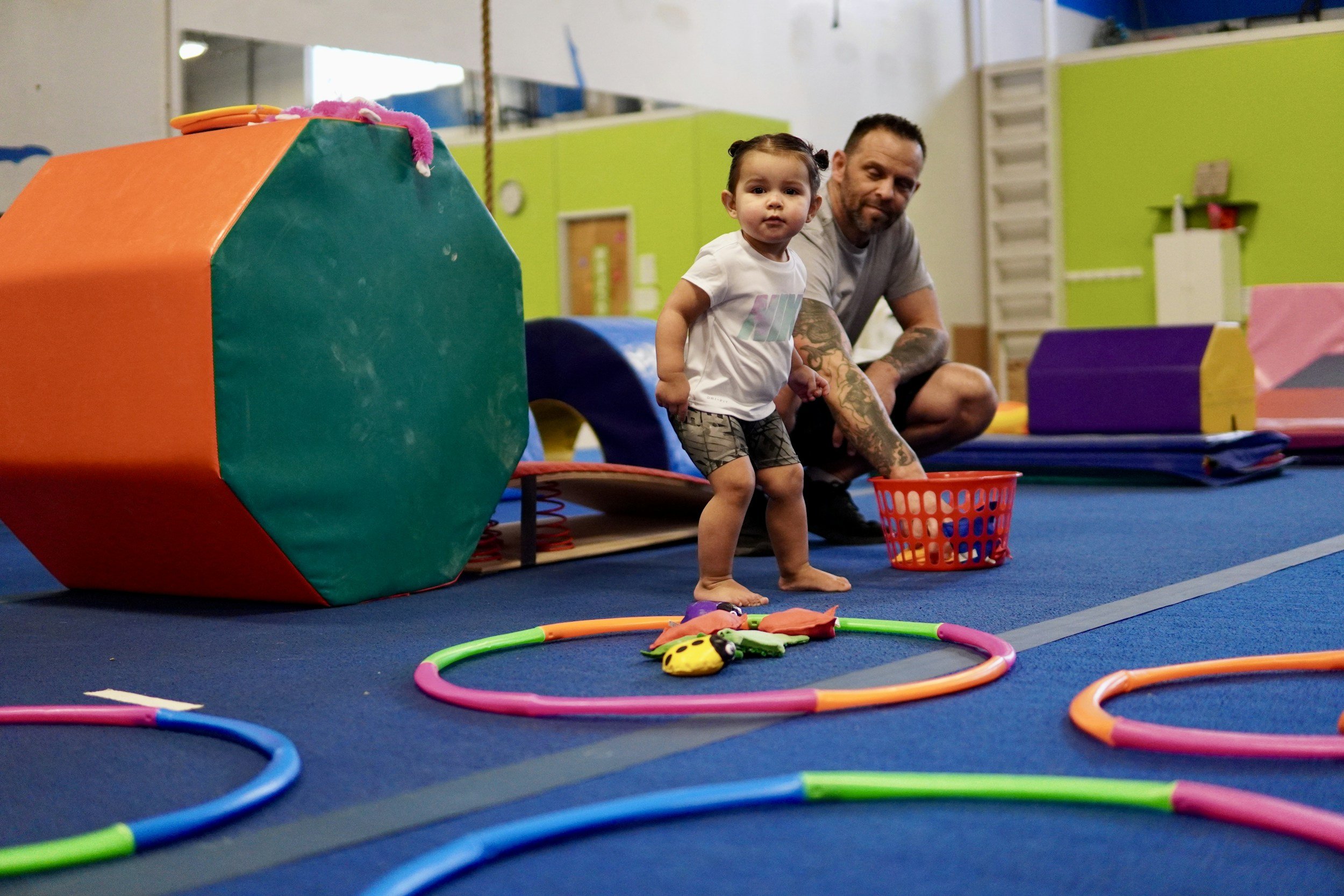 Child and adult playing in a colorful indoor gym with foam blocks and toy hoops.