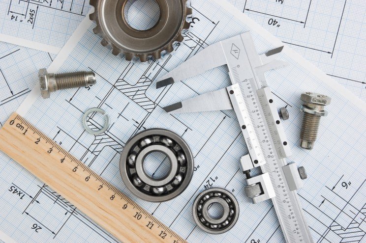 Assorted metal mechanical parts, bearings, bolts, and rulers on technical blueprints.