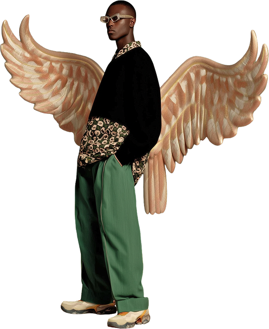 Person wearing glasses, a black sweater with patterned sleeves, green pants, and sneakers, standing in front of a digital illustration of large angel wings.