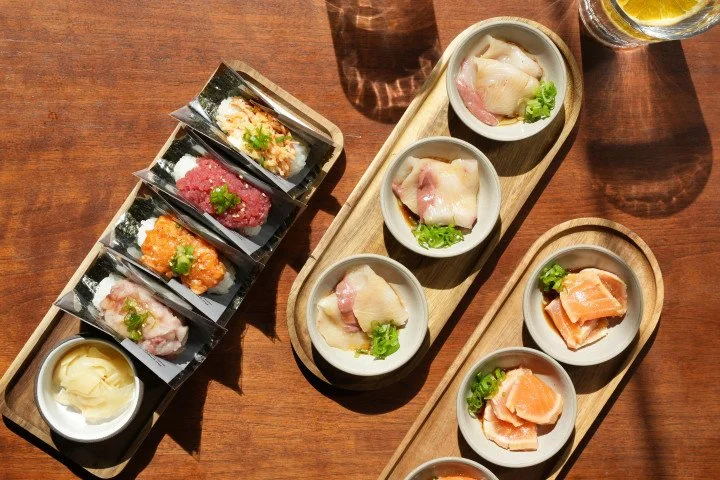 Assorted sushi on wooden trays, including nigiri with fish, and rolls with various toppings, served with wasabi and pickled ginger on a wooden table.