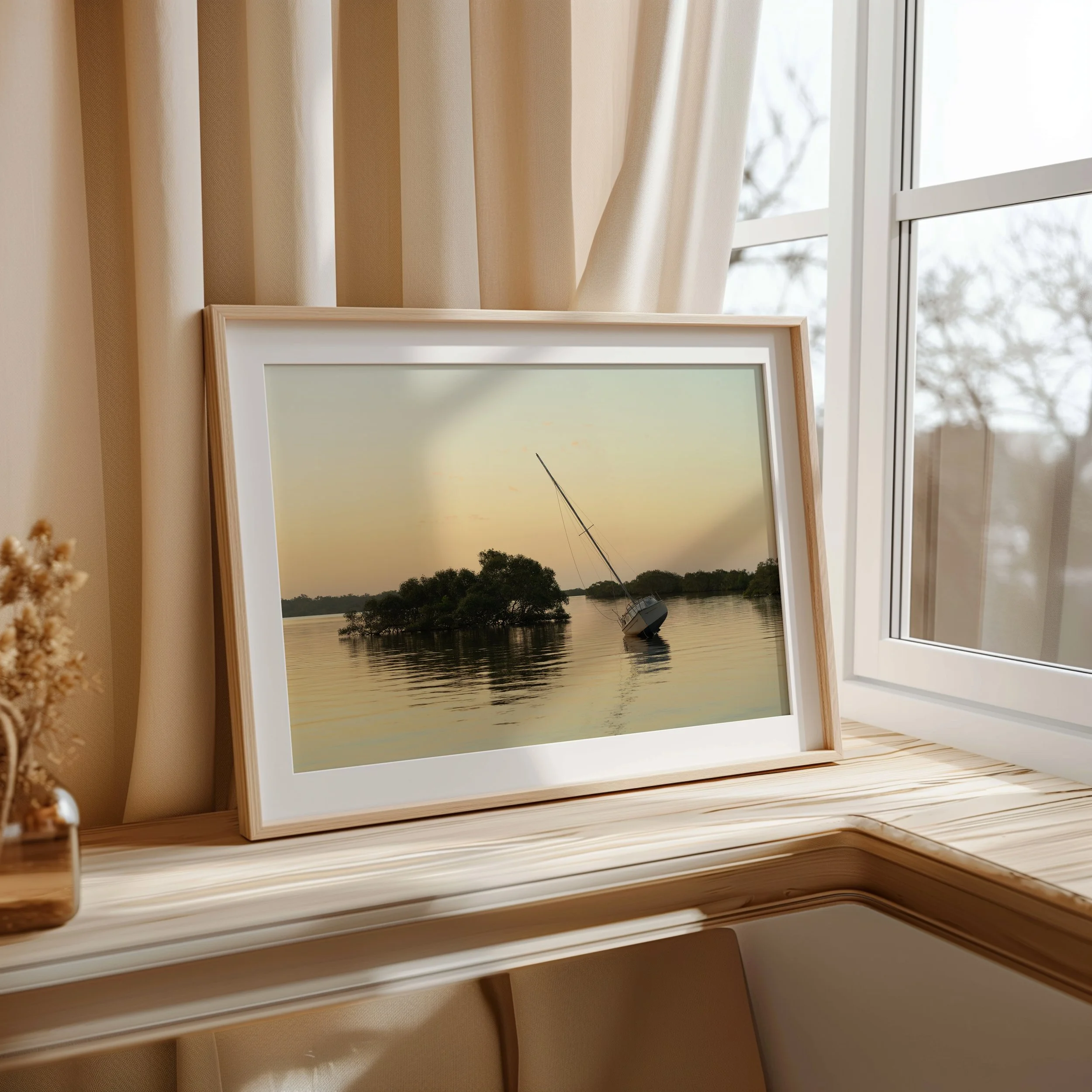 Framed sunset sailboat photograph displayed next to a window
