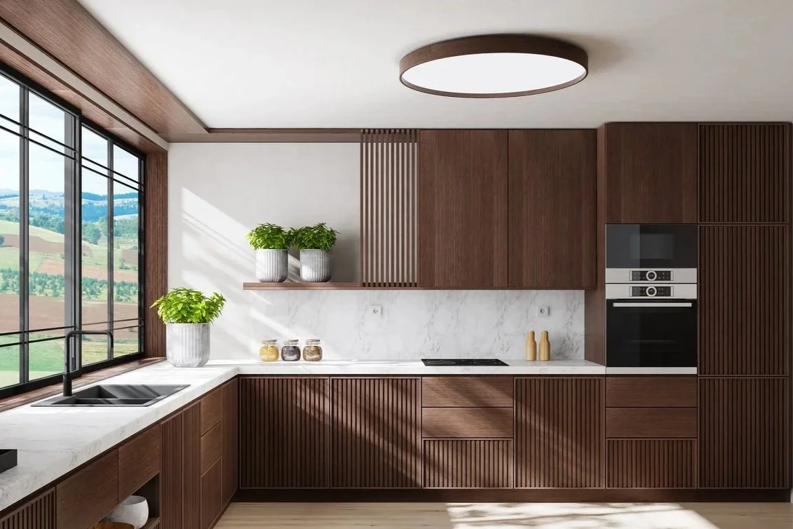 Modern kitchen with wooden cabinets, white marble countertops, large window with scenic view, potted plants, and built-in oven.