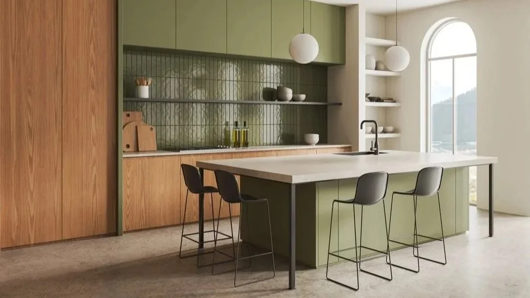 Modern kitchen with green cabinets, a large island with a white countertop, black bar stools, and hanging pendant lights near a large arched window.
