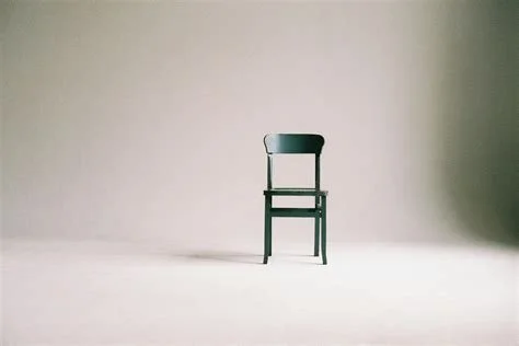 A single dark chair in the center of a plain, light-colored background.