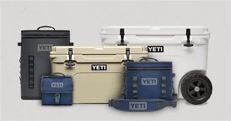 Collection of YETI coolers and ice chests in black, cream, navy blue, and white, with some featuring wheels and handles.