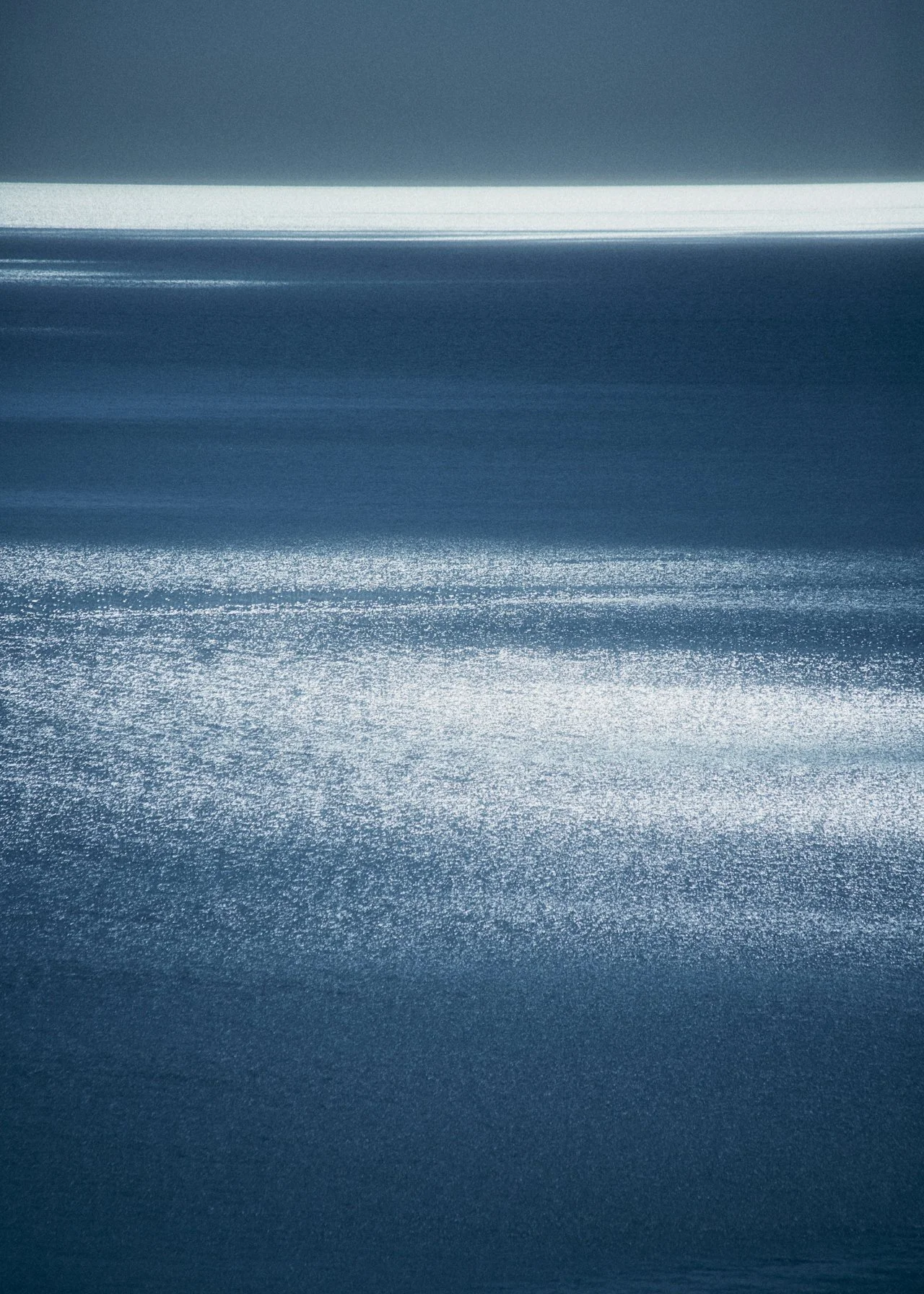 Abstract image with shades of blue, featuring a horizontal white line across the top and sparkling reflections on a dark blue surface below.