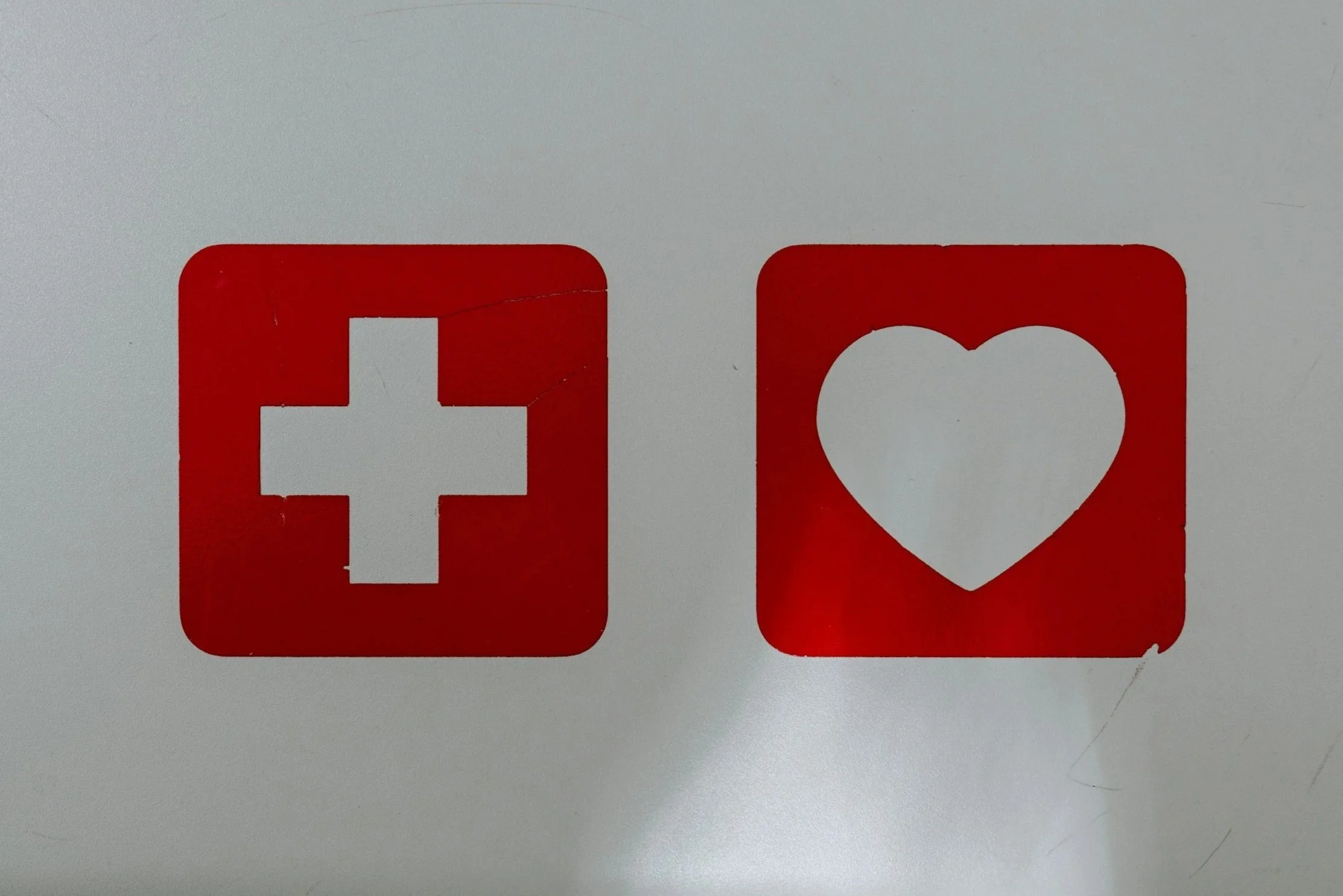 Red and white social media icons, with a red square featuring a white cross on the left and a white heart on the right, on a white background.