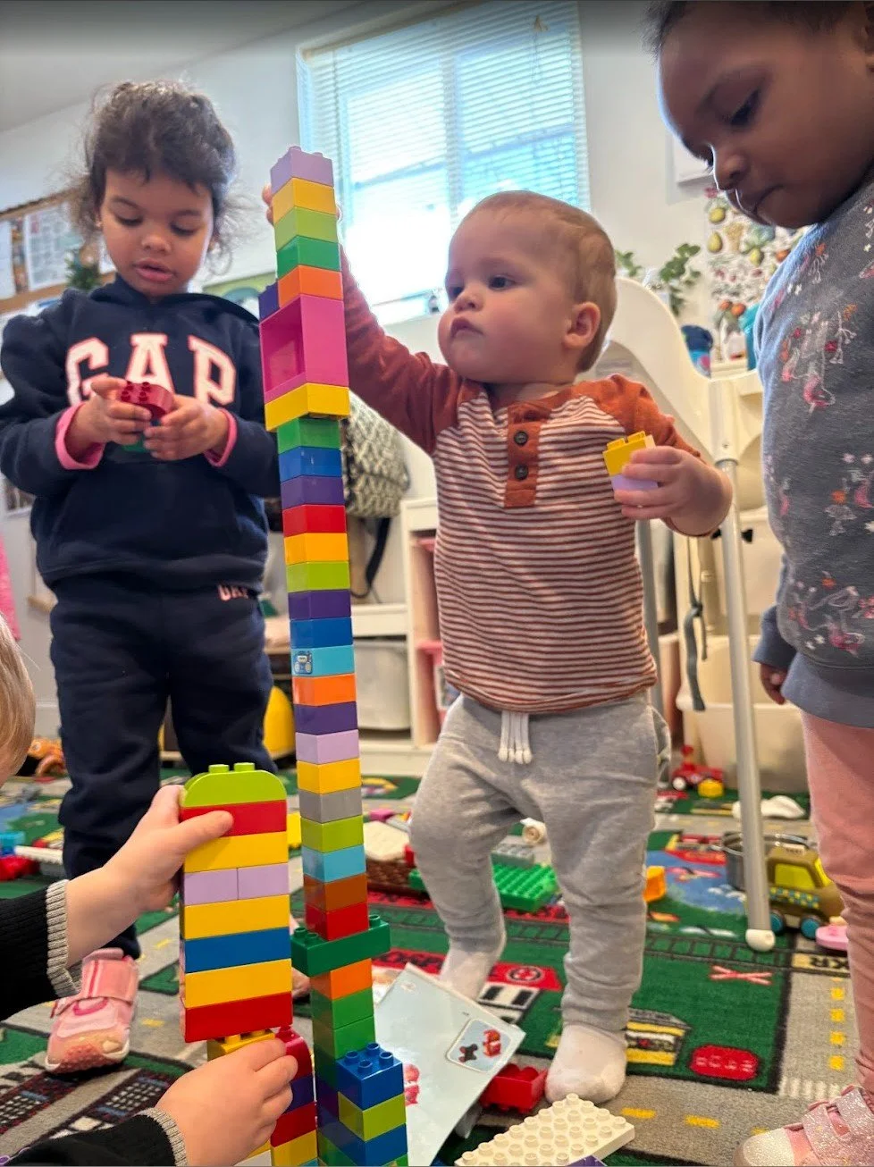 Children playing with colorful building blocks on a playmat indoors.