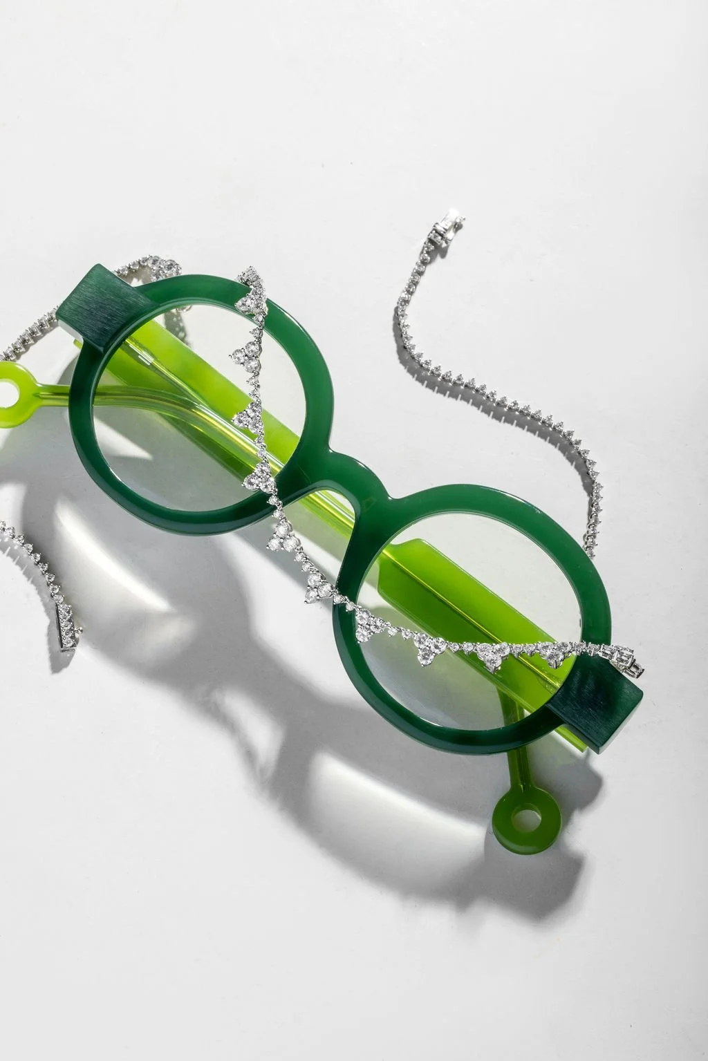 Gafas de sol verdes con cadenas de cristales y un collar de cristales, sobre un fondo blanco.
