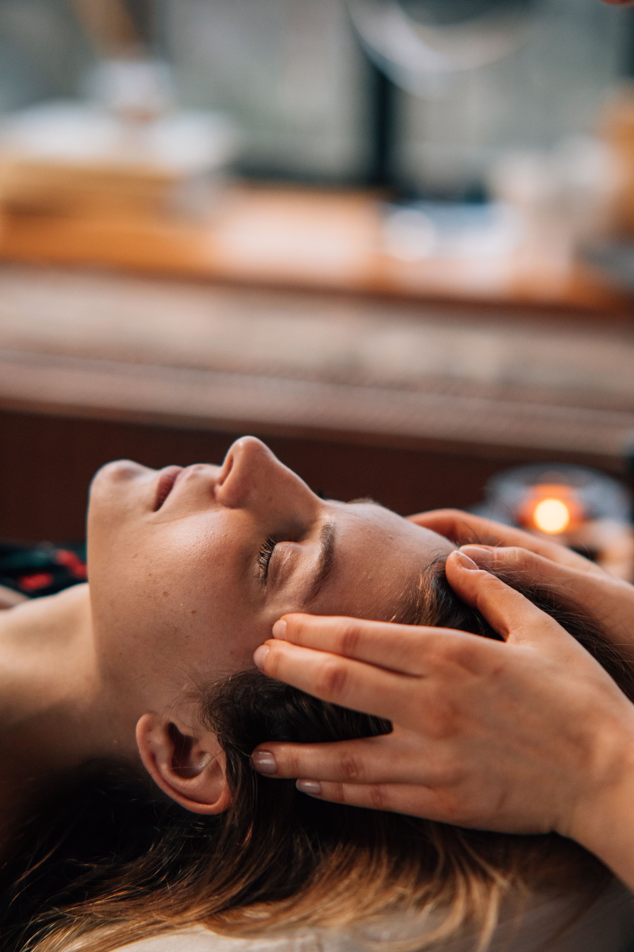 A woman receiving craniosacral therapy, lying with eyes closed, with a therapist's hands gently at her temples.