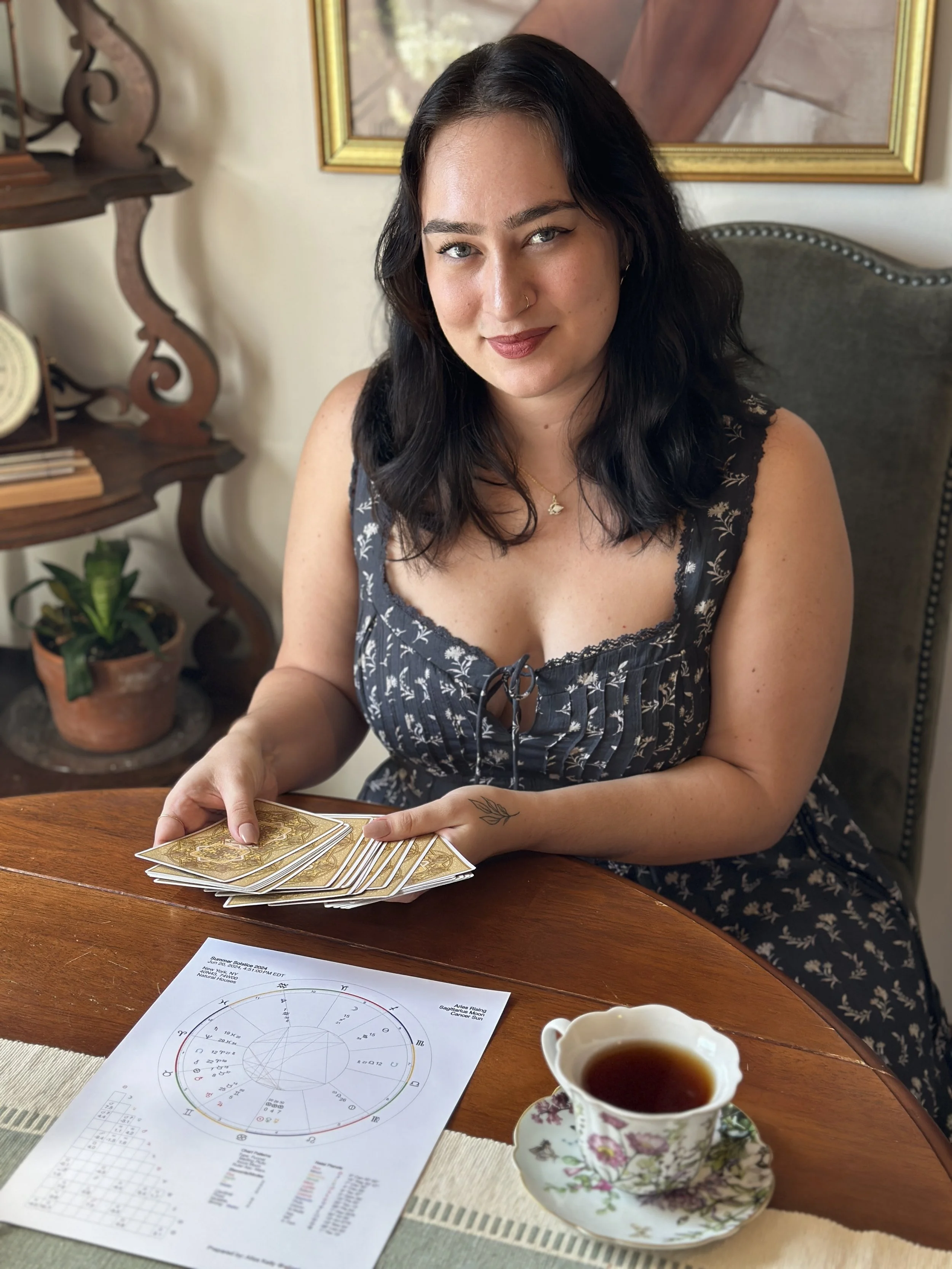 Hands holding Tarot deck cards and hovering over a birth chart reading for astrology