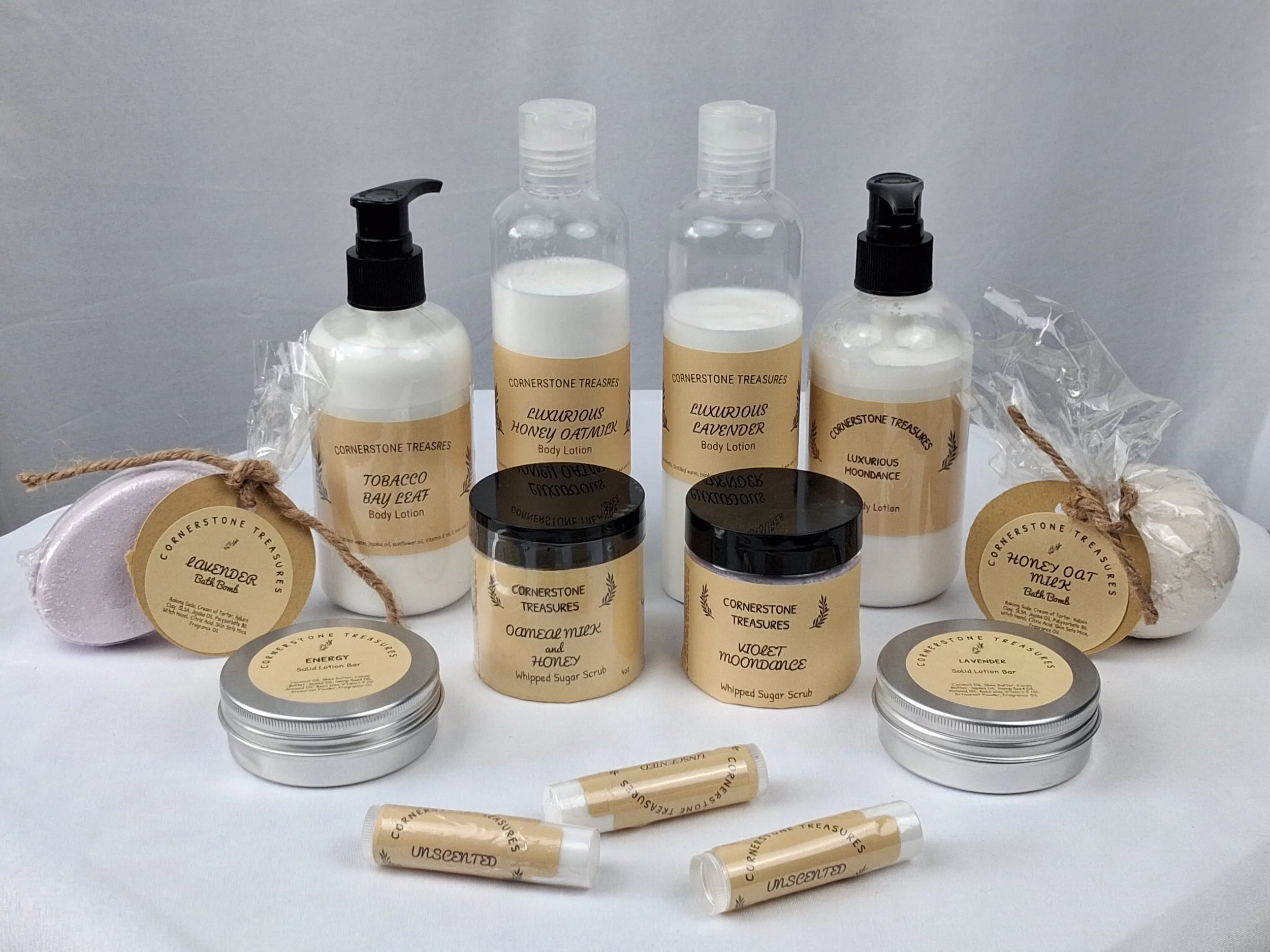 A collection of personal care products including body lotions, bath bombs, and whipped sugar scrub bottles from Cornerstone Treasures, arranged against a plain background.