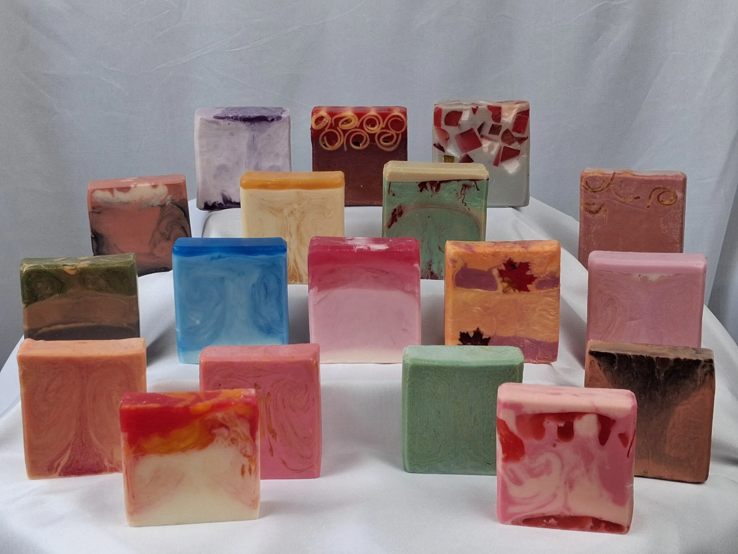 Colorful handmade soap bars arranged in multiple rows on a white display.