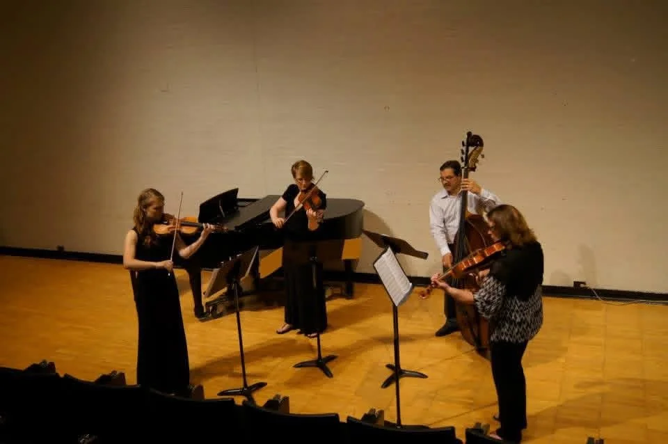 Four musicians performing on stage: a pianist, two violinists, and a double bass player.