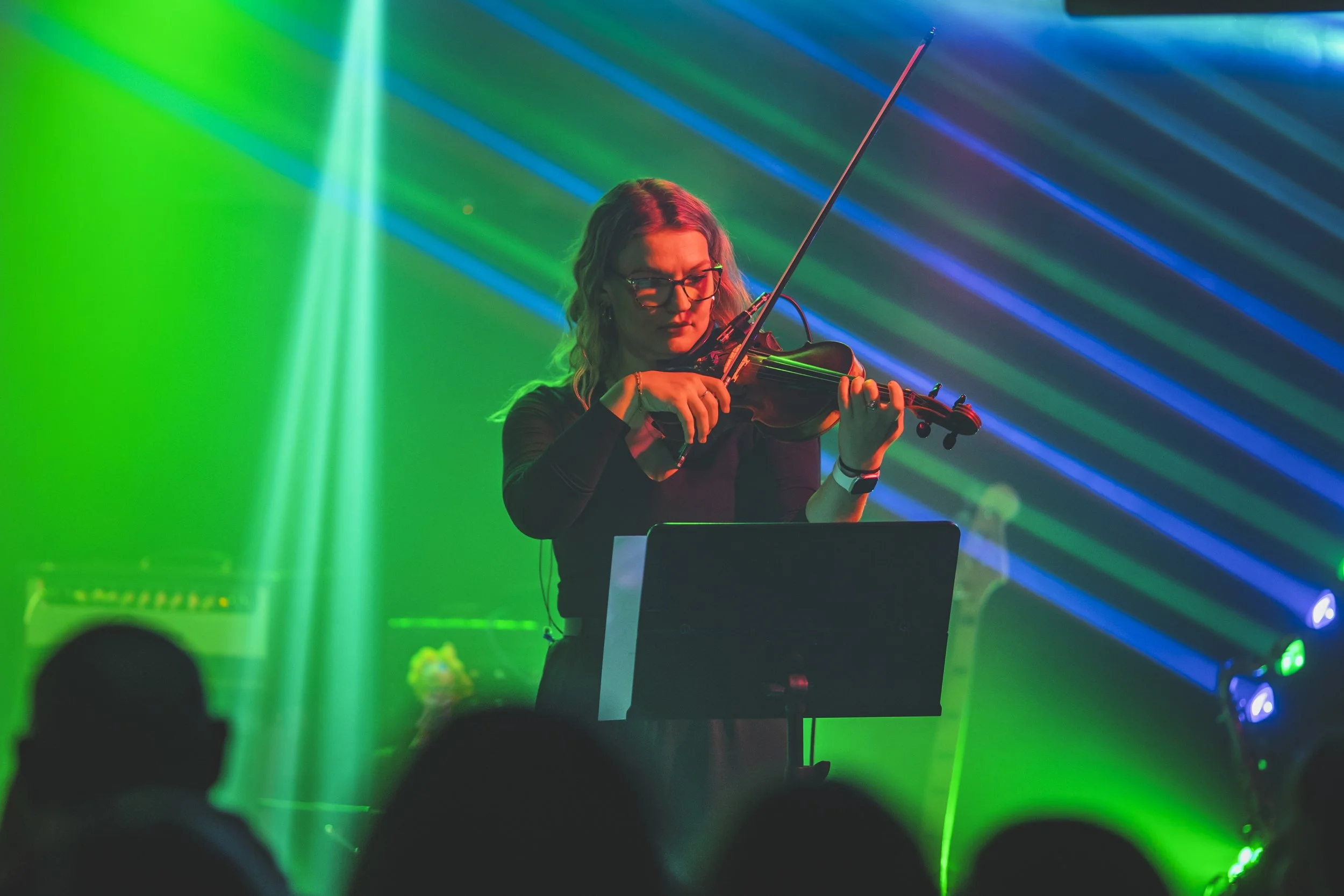 A woman playing the violin in front of colorful laser lights at a concert or event.