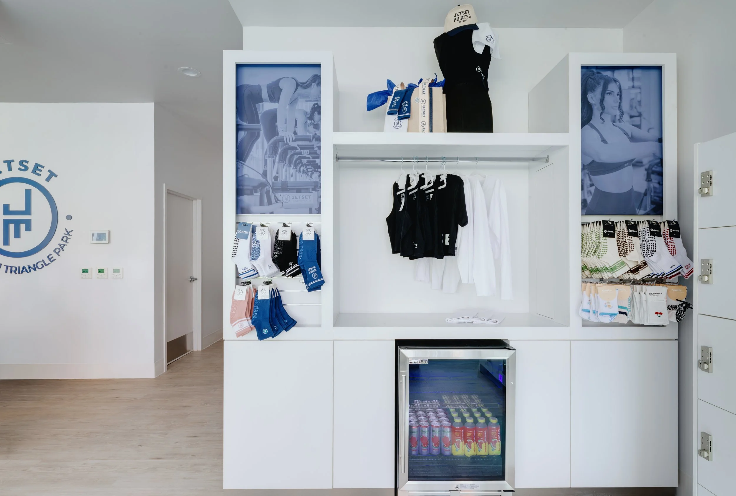 A retail display shelf with athletic clothing, socks, and a mini fridge with beverages in a modern, well-lit store.