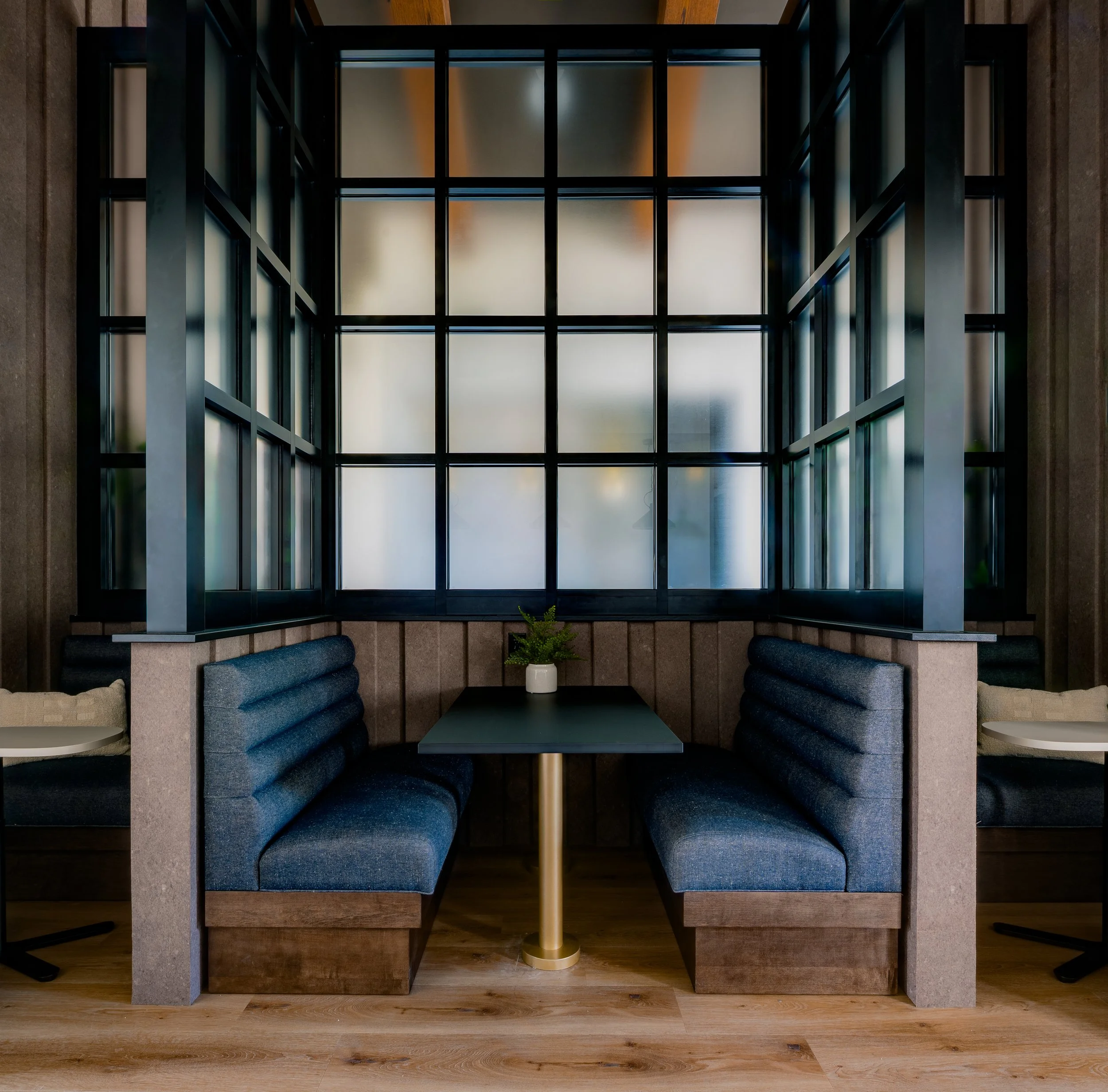 Interior view of a modern stairwell with black metal framing, frosted glass panels, a small table with a white potted plant, and blue cushioned seating along the walls.