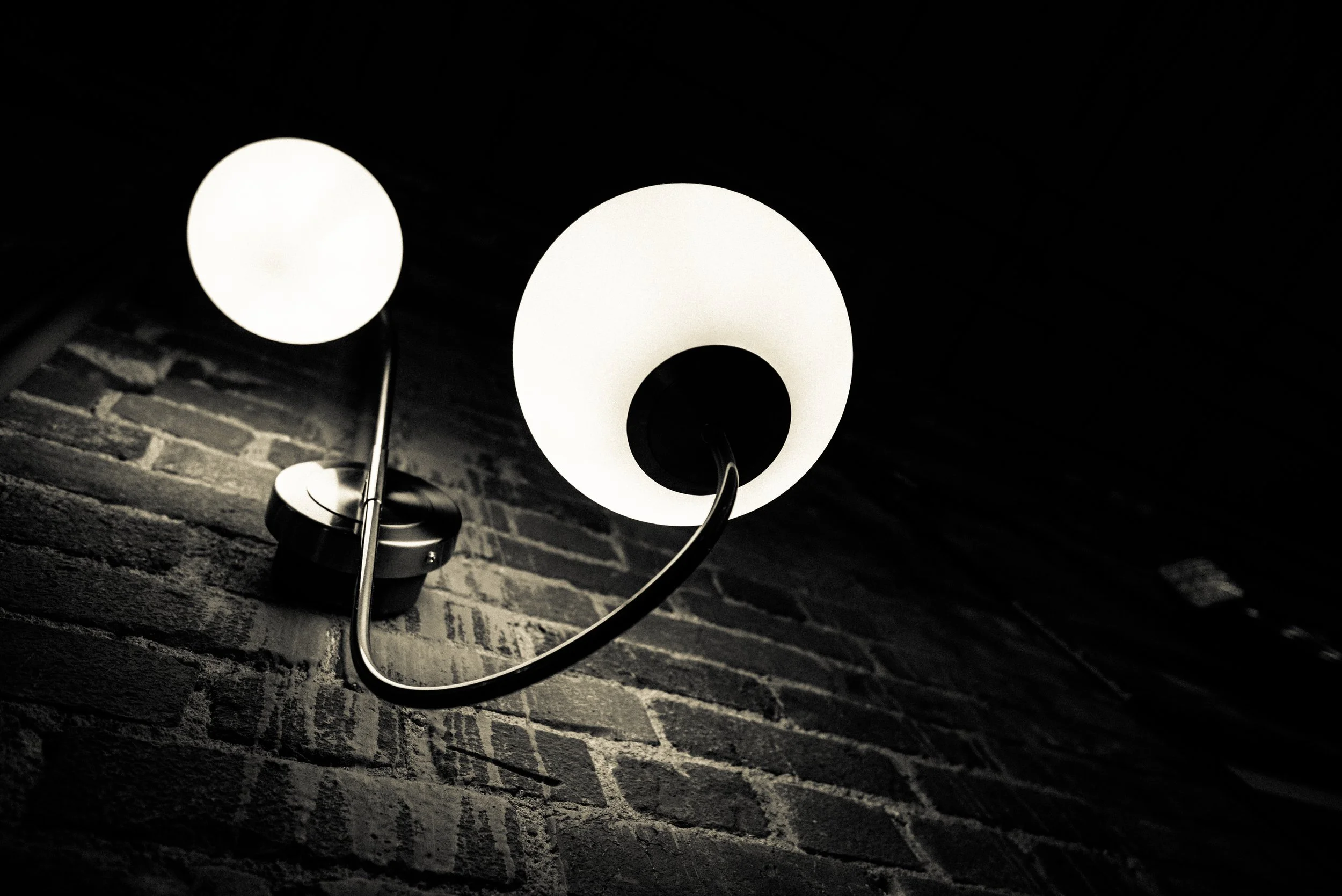 Close-up of two modern wall lamps with white, dome-shaped shades mounted on a brick wall in a dimly lit room.