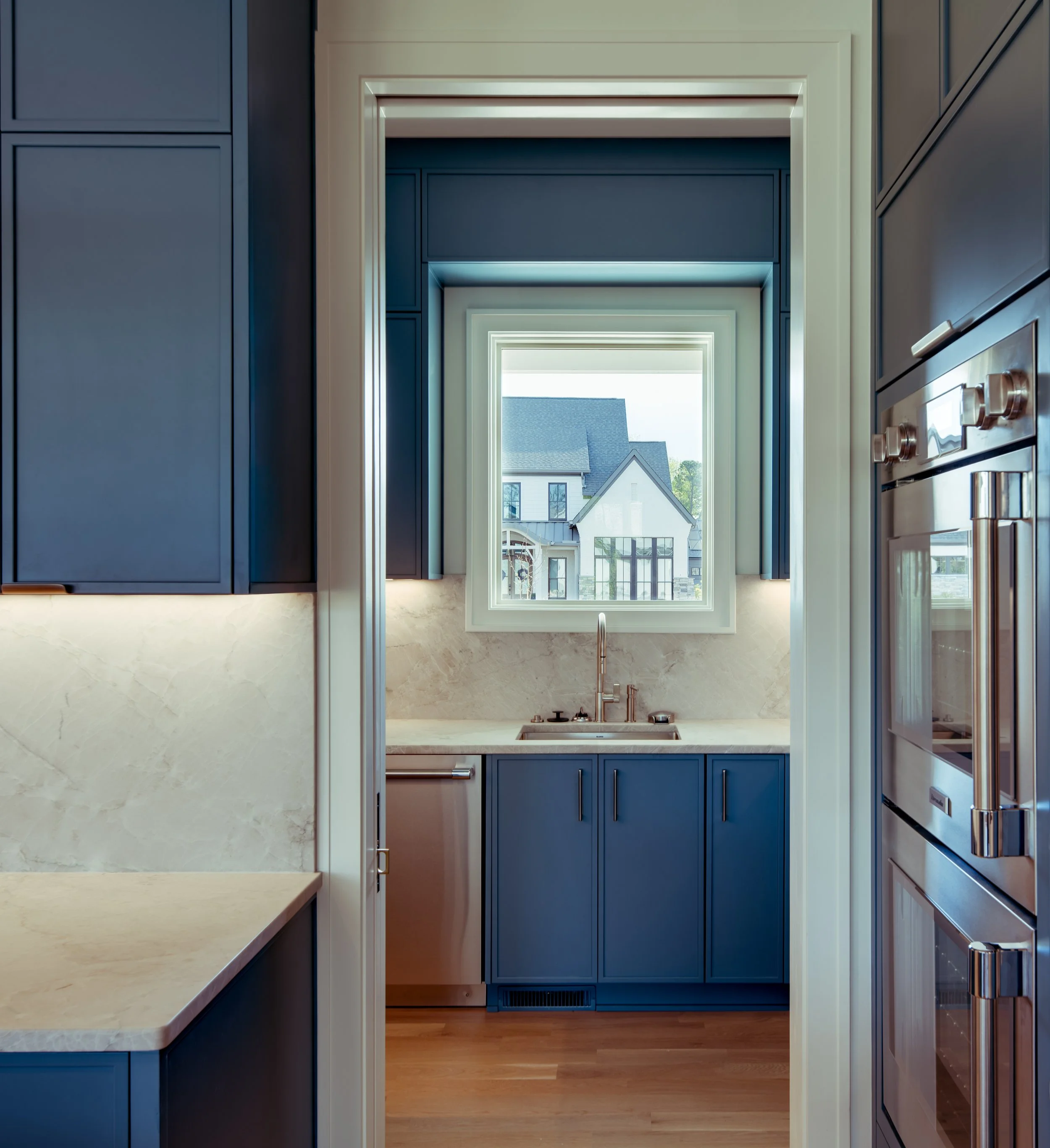 A view through kitchen cabinets showing a window and houses outside.