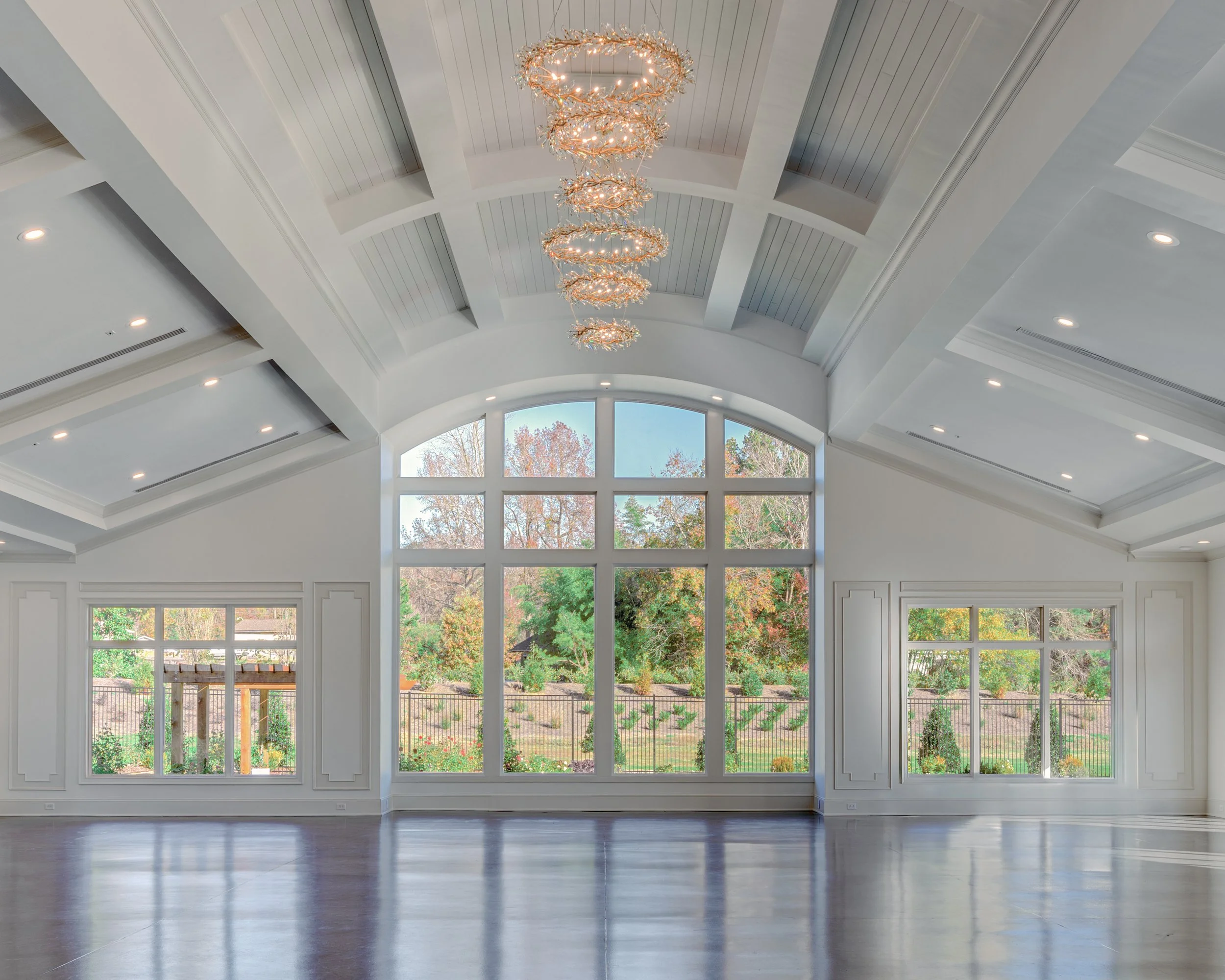 Spacious room with large windows, high vaulted ceiling, and a decorative chandelier hanging from the ceiling.
