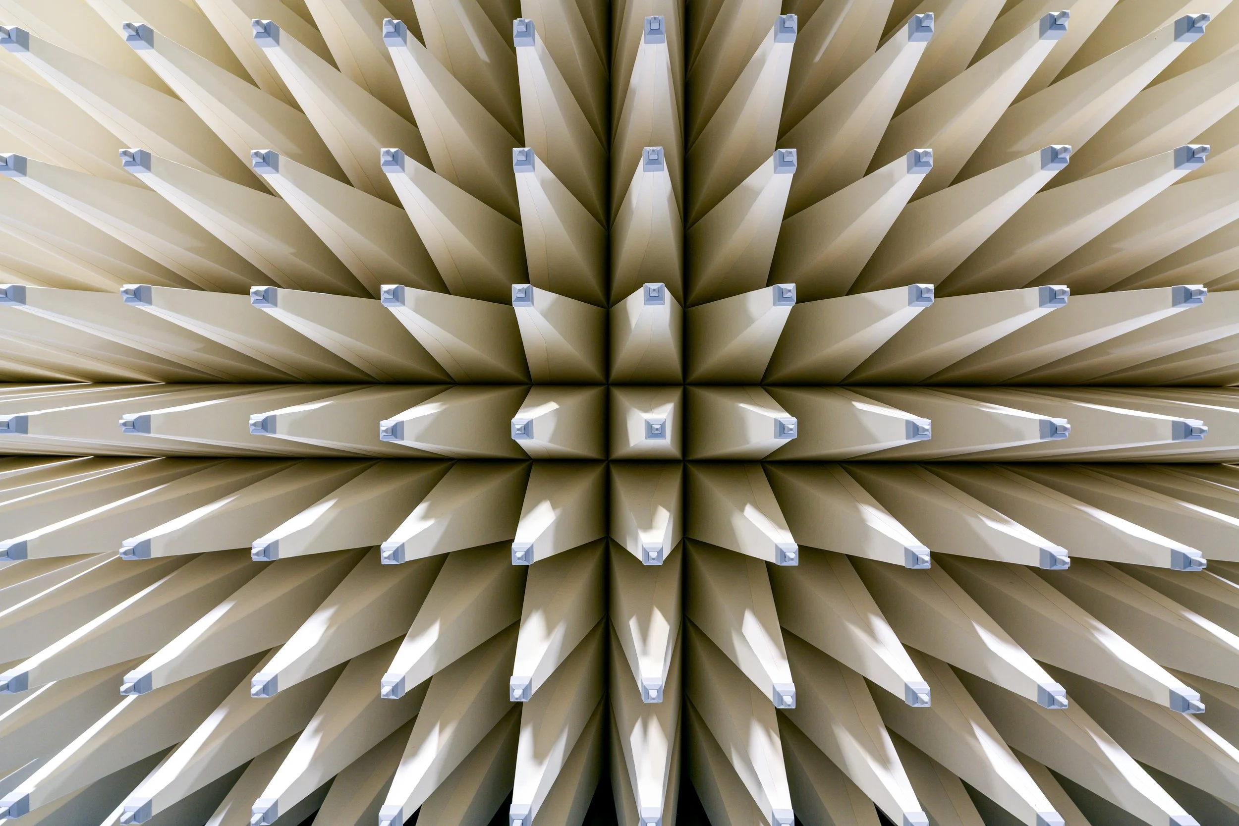 Close-up of neatly arranged beige or light-colored rectangular objects with blue tabs on the top, viewed from below, creating a pattern of repeating shapes.