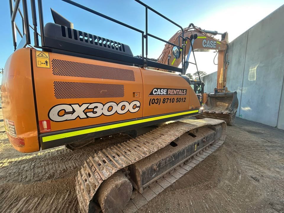 Orange CASE CX30C excavator with black tracks, positioned on dirt next to a concrete wall, with a lifting platform and hydraulic arm extended.