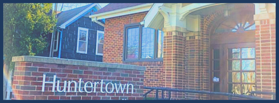 Close-up of a brick building with a sign that reads 'Huntertown'. The building has windows, an entrance with a decorative awning, and a curved brick wall.