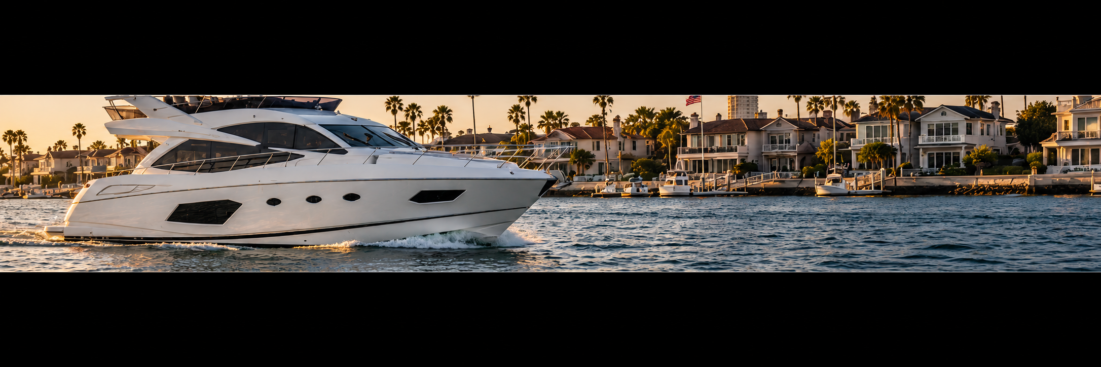Luxury white yacht managed by Coastal Peace of Mind's Yacht Charters, sailing in a Newport Beach marina with waterfront houses and palm trees in the background during sunset.