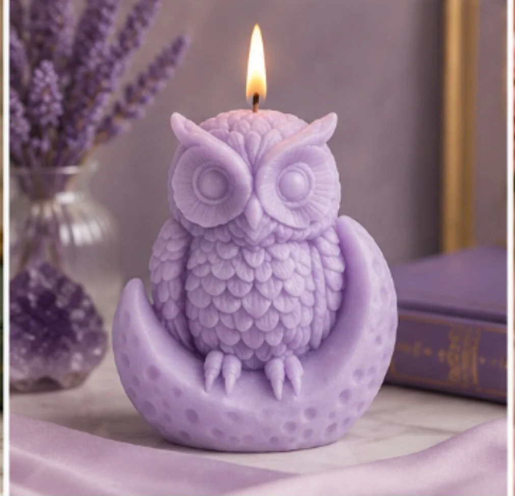 A lavender-colored owl-shaped candle with a lit flame on its head, placed on a decorative surface with lavender flowers and books in the background.