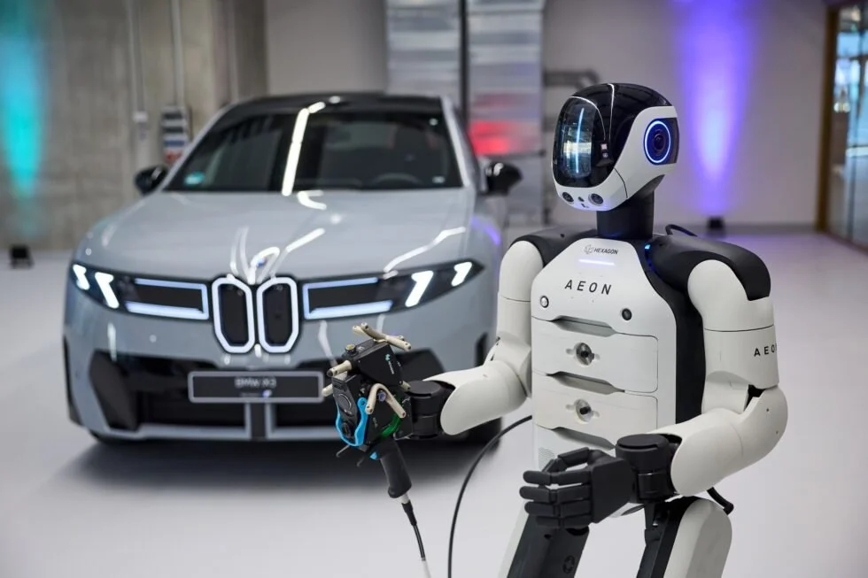 A robot with a humanoid design holding a tool, with a white and black luxury BMW i3 car in the background inside a modern showroom.